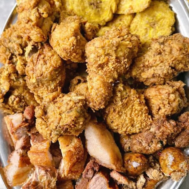 Picada mixta con trozos de pollo frito crujiente, chicharrón, carne asada y rodajas de plátano frito servidos en una bandeja metálica
