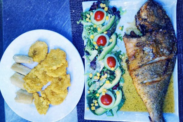 Pescado frito entero acompañado de patacones de plátano y ensalada fresca con aguacate, tomate cherry y maíz servido en platos blancos