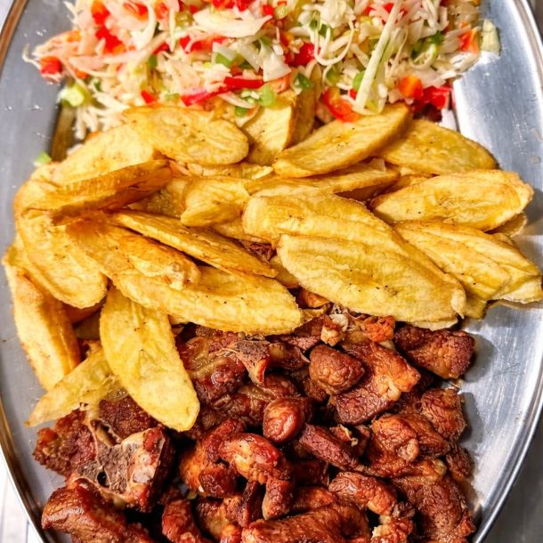 Chicharrón de cerdo crujiente acompañado de plátanos fritos y ensalada fresca de repollo, pimiento y cebolla servido en bandeja metálica